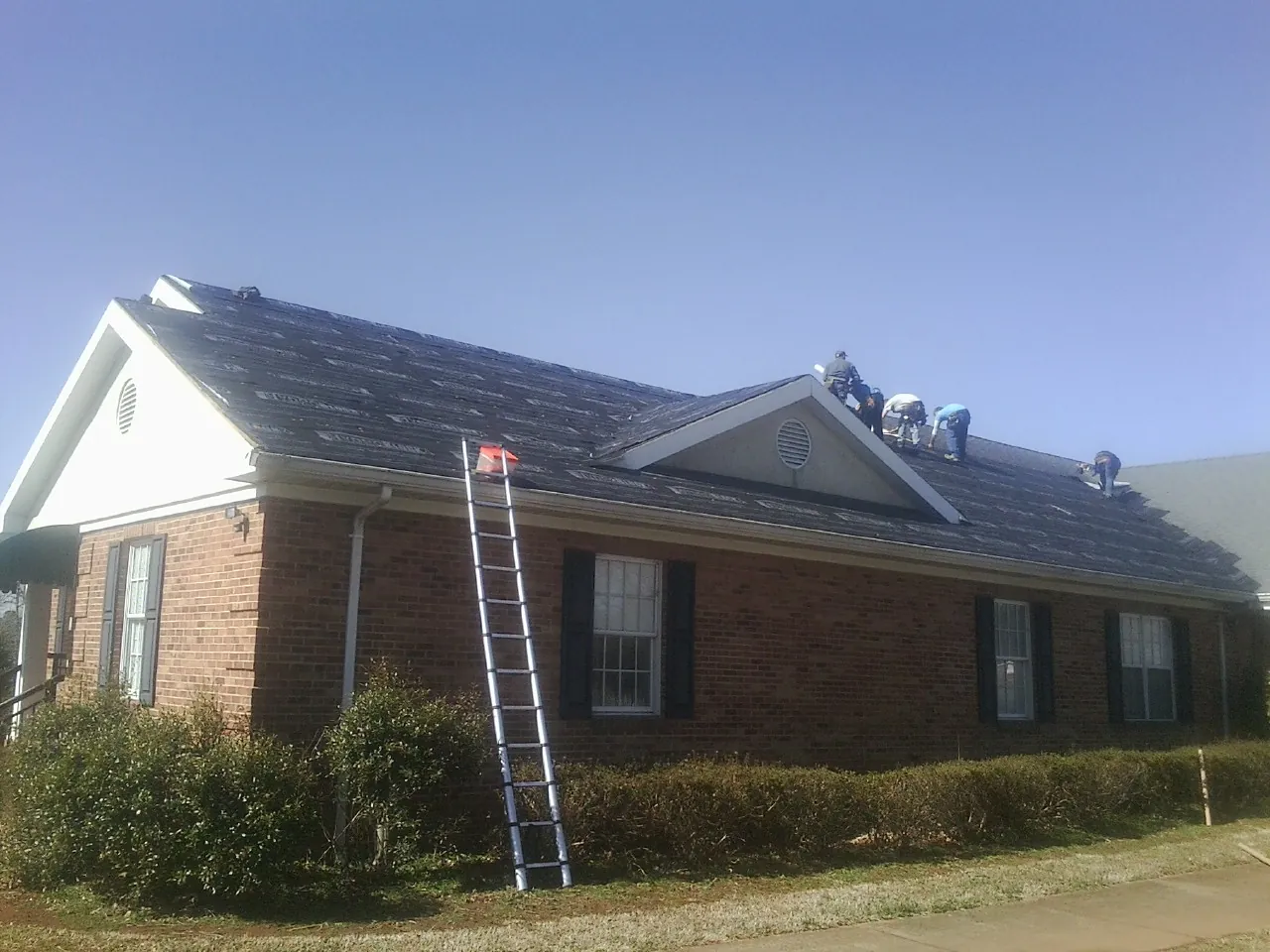 Crew tearing shingles off a brick ranch roof with a ladder set — Emergency Roof Repair work by our crew in Uniontown